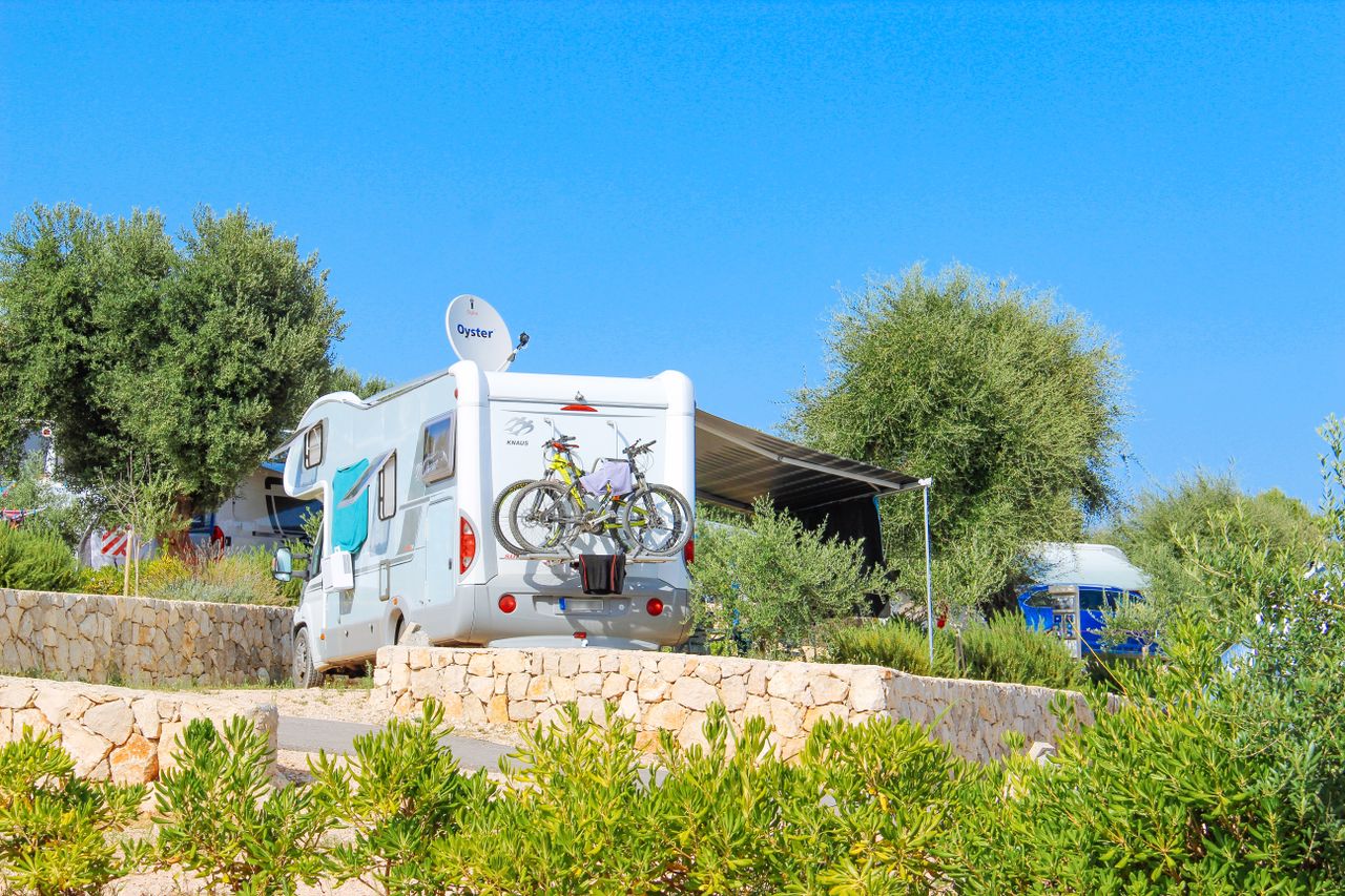 Camper van with bicycles parked at a campsite under blue skies in Croatia.